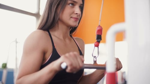 Young Woman Flexing Muscles On Cable Gym Machine