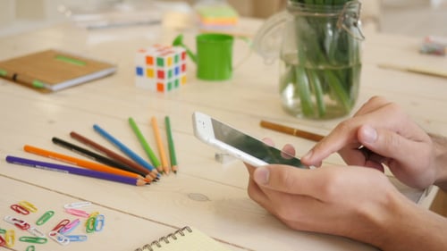 Hands Scroll on Phone at Creative Workspace