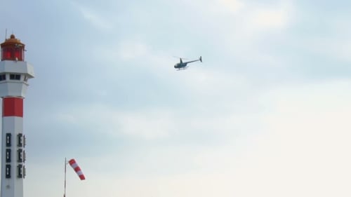 Helicopter Flying Near Coastal Lighthouse on Cloudy Day