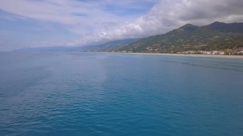 Drone flies over sea surface, aerial of waves reaching shore, sea coast village and mountains