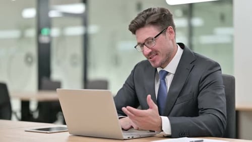 Cheerful Middle Aged Businessman Talking on Video Chat on Laptop in Office