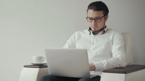 Junger Mann in Brille trinkt Kaffee, während er Laptop benutzt. Weißer Hintergrund.