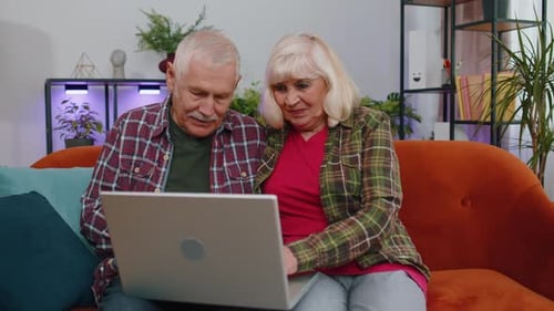 Senior Grandmother Grandfather Using Laptop Computer Typing at Home Room Looking at Camera Smiling