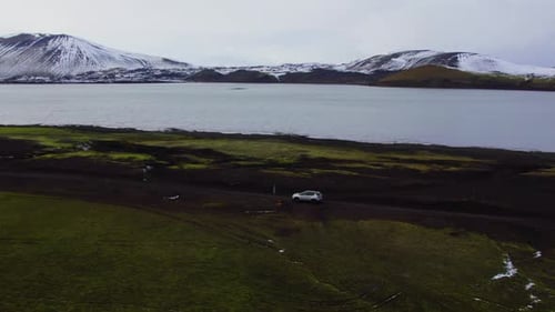 Aerial of a Car Driving on Dirt Road Along Lake and Majestic Mountains Iceland