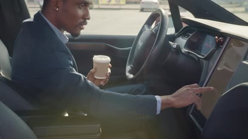 Vista lateral del hombre africano concentrado sentado en el asiento del conductor con taza de café y