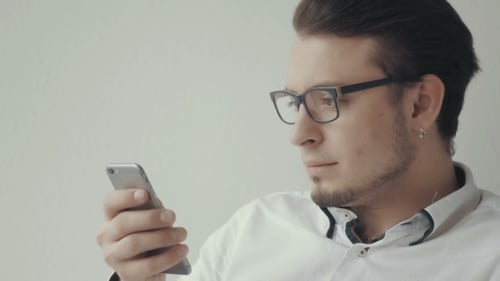 Portrait Of Young Man In Glasses Using Cell Phone Against White Background