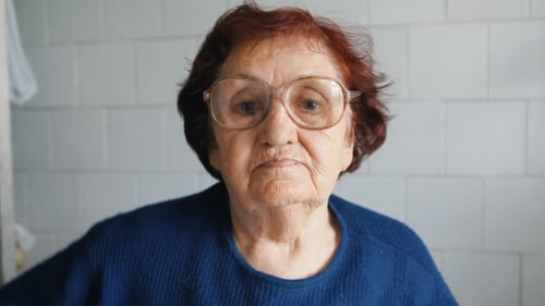 Senior Woman Puts on Glasses Indoors, Close Up