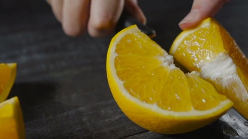 Cutting Fresh Juicy Orange with Knife in Kitchen