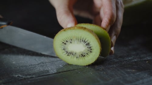 Chefkoch schneidet Kiwi auf Holztisch mit tropischen Früchten