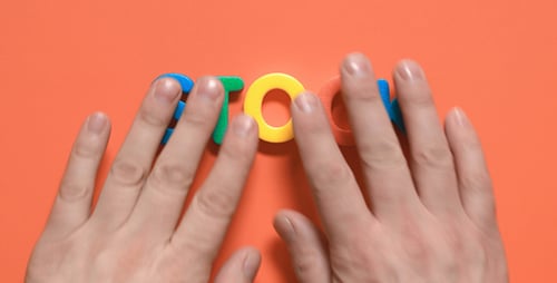 Hands Manipulate Colorful Clay Letters on Orange Surface