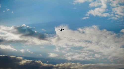 Drone Flying Silhouetted Against Cloudy Blue Sky