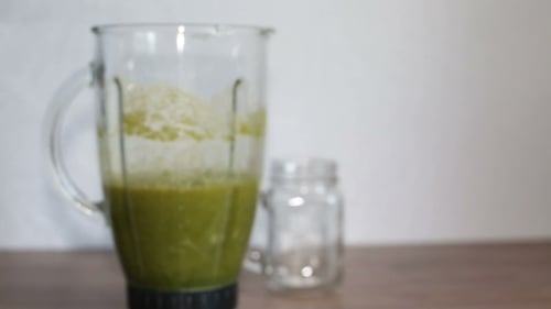 A Blender Jar With Green Healthy Smoothie And a Mason Jar On a Wooden Table