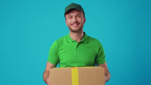 A Young Male Courier in a Green Uniform Holds a Parcel in His Hands