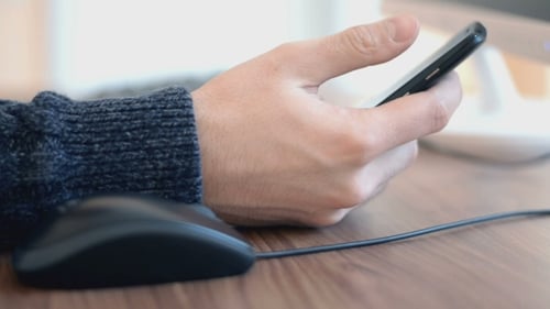 Man Using Mouse and Smart Phone at Desk