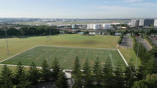 Aerial forward flying toward a soccer, football, rugby field with airport in the background