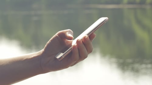 Hand Scrolling on Mobile Phone Near Water
