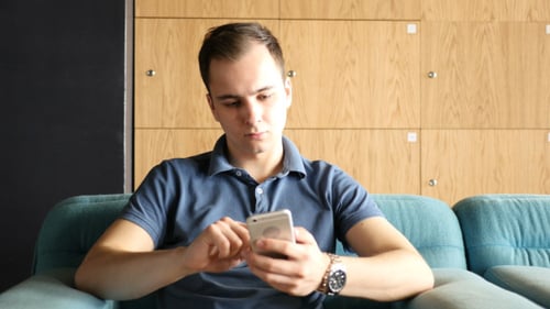 Young Man Using Smartphone while Sitting on Sofa