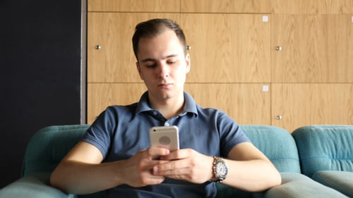 Man Texting on Smartphone while Sitting on Sofa