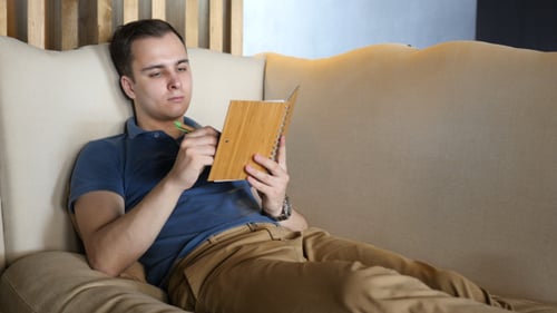 Young Man Relaxing, Writing in a Notebook on Couch
