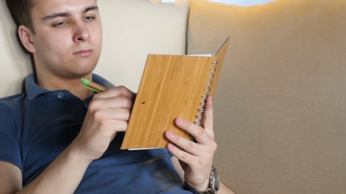 Young Adult Writing in Notebook on Couch