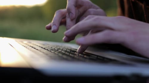 Hands Typing on Laptop Keyboard at Sunset