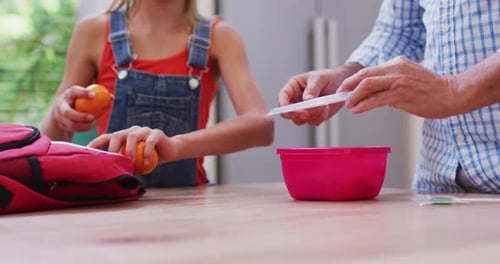 Child and Senior Packing Lunchbox Together in Kitchen