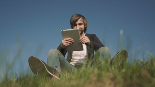 Bottom View Of Young Man Talking On Skype Using a Tablet PC Sitting On The Grass