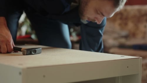 Mann baut Möbelteile mit einem Hammer zusammen