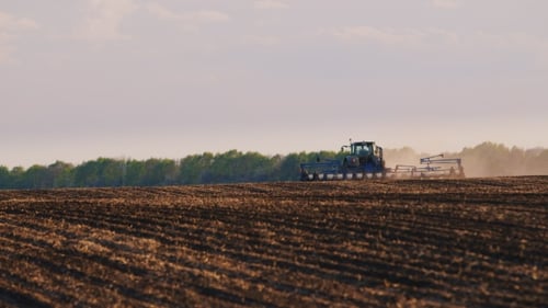 Tractor Working In a Field In The Foreground Of Uncultivated Land For Sowing