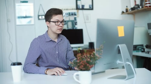 Happy Young Man, Wearing Glasses And Smiling, As He Works On His Laptop