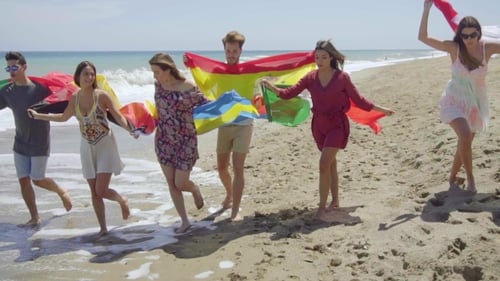 Young Adults Running on Beach Holding Flags