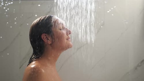 Hübsche Brünette mit langen nassen Haaren steht unter Duschdüsen