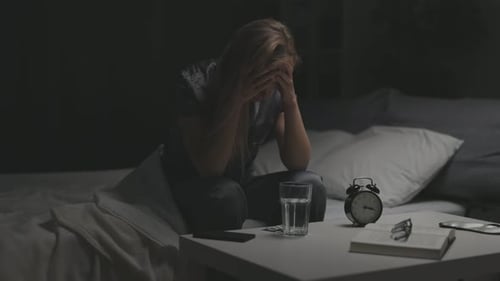 Woman Sits on Bed With Head in Hands