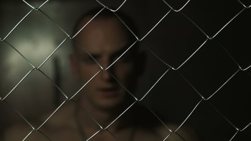Bald Man Behind Wire Fence in Dark Lighting