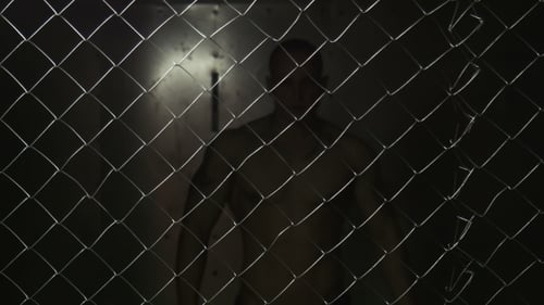 Muscular Man Behind Chain Link Fence at Night