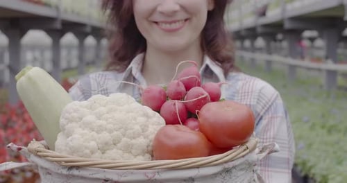 Mujer sonriente irreconocible mostrando una cesta con rojizo, tomate y repollo ante la cámara. Retrato de