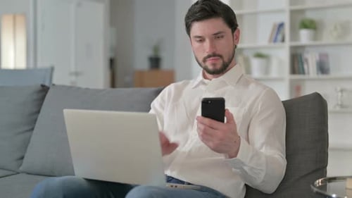 Man Using Smartphone and Laptop While Sitting on Sofa