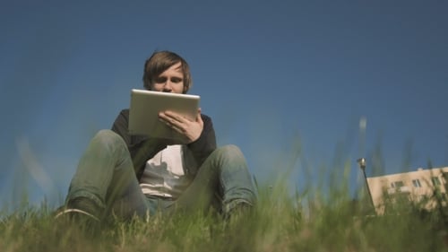 Man Uses Tablet Outdoors in Green Grass