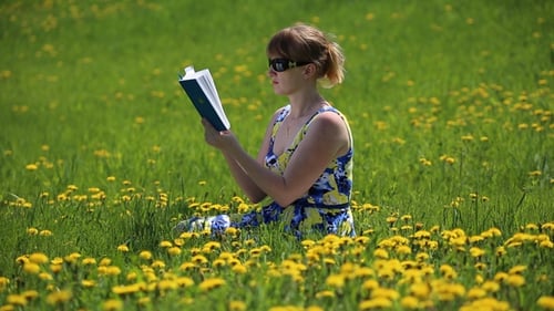 Woman Reading Book Sitting Among Dandelions in Field