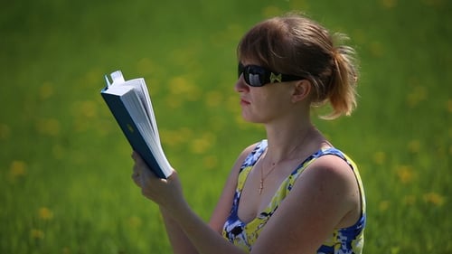 Woman Reads Book on Green Field in Sunlight
