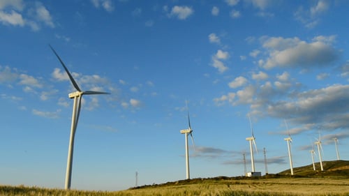 Wind Turbines Spin on a Hillside on Sunny Day