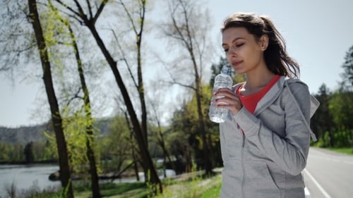 Active Woman Drinks Water After Exercise in Park