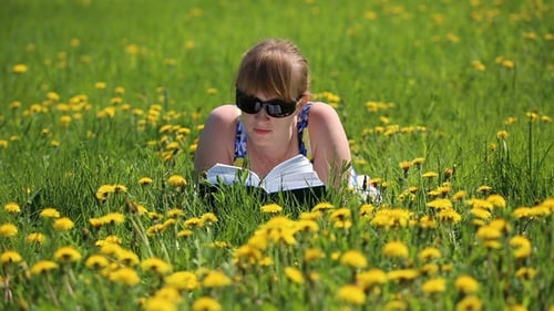 Woman Reading Book Lying in Grassy Dandelion Field