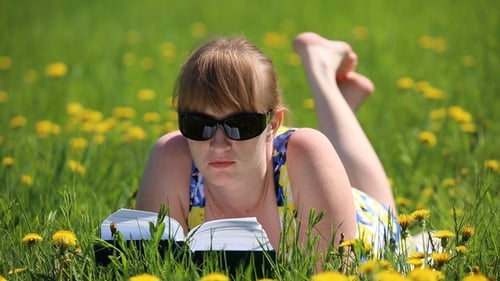 Woman Reading Book Lying in a Sunny Meadow