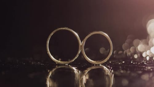 Wedding Rings on Dark Water Surface Shining with Light. Close Up Macro