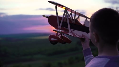 Boy Holds Homemade Airplane On Sunset Background On Rock.