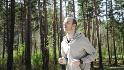 Man Jogging and Checking Smartwatch in Forest