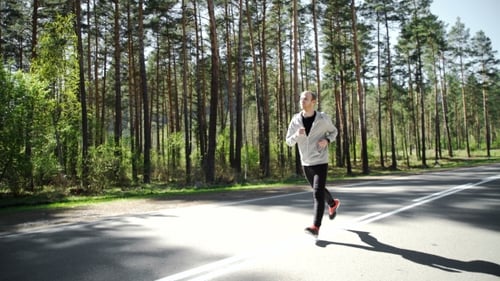 Young Adult Runs on Forest Road on Sunny Day