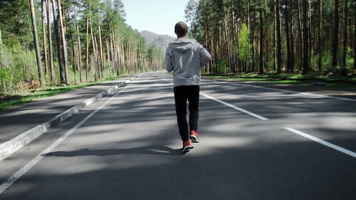 Man Runs on Road Through Green Forest