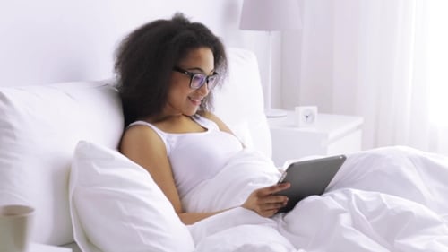 Woman Relaxes in Bed with Tablet Technology